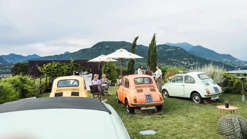 Eine Gruppe von Autos, die auf einer Wiese geparkt sind, mit Menschen, die herumstehen.