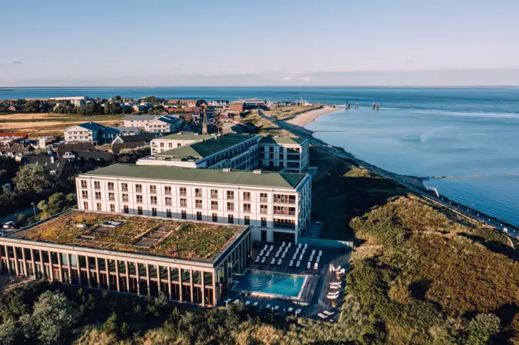 Luftaufnahme des A-ROSA Hotels auf Sylt mit Pool und einem Strand im Hintergrund.