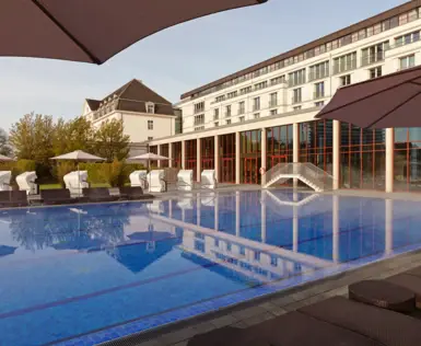 Swimmingpool mit Sonnenschirmen und Stühlen vor einem Gebäude.