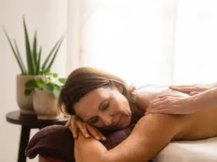 Un massaggio benessere rilassante in un ambiente termale, dove le mani della massaggiatrice scivolano delicatamente sulla schiena di una donna sdraiata su un lettino da massaggio.