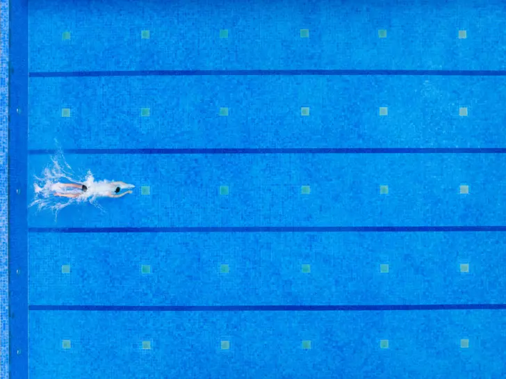 Eine Draufsicht auf eine Person, die im klaren, blauen Wasser eines Schwimmbeckens mit markierten Bahnen schwimmt.