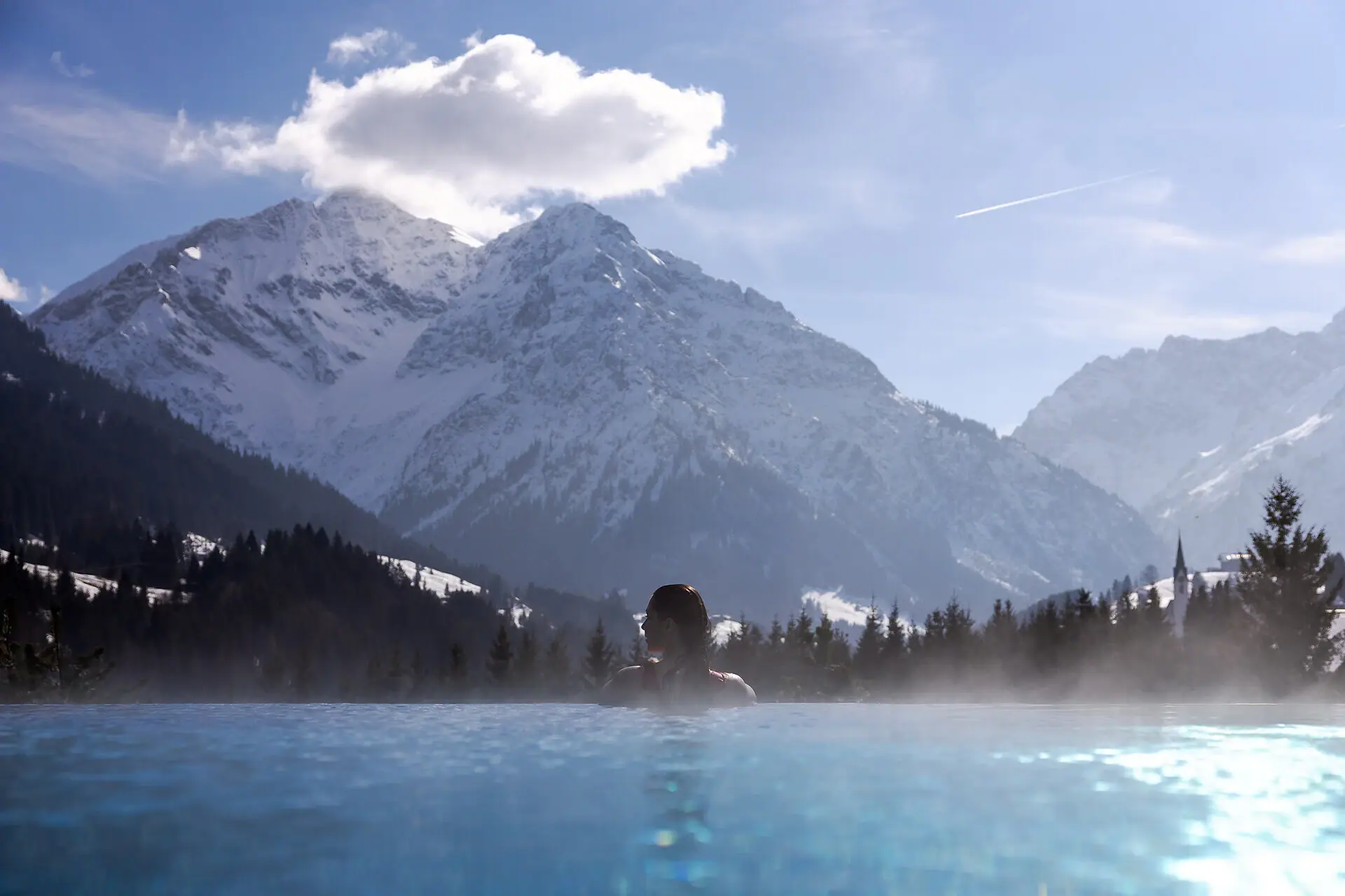 Außenpool in Winter Eine Person im Pool mit Bergen im Hintergrund.