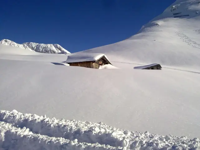 A snow-covered mountain landscape with two snow-covered cottages.