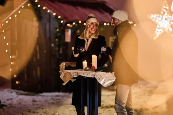 Ein Mann und eine Frau stehen im Winter draußen mit Kerzen und Lichtern.