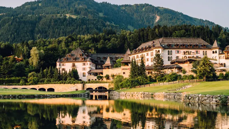 Ein Gebäude in der Nähe eines Sees mit Bäumen und Bergen im Hintergrund.