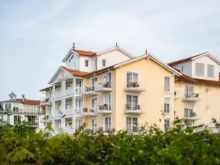 Das gelbe Gebäude des A-ROSA Ostseehotel Kühlungsborn ragt hinter einer grünen Hecke hervor.