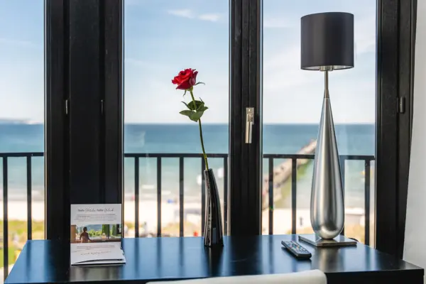 Blick vom Hotelzimmer auf den Strand durch große Fenster, mit sichtbarem Himmel und Ozean.