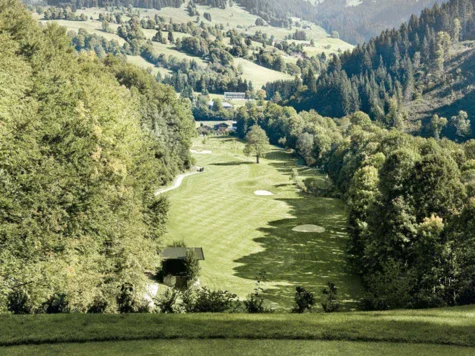 Die Ansicht des Golfplatzes von einem Hügel inmitten von grünen Wäldern. 