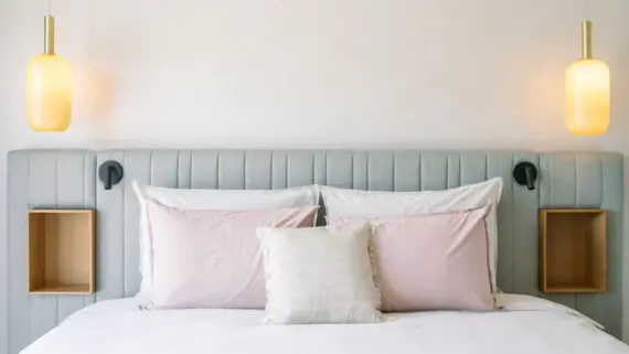 Cozy hotel bedroom featuring a neatly made bed with plush pillows and two elegant bedside lamps hanging from the ceiling.