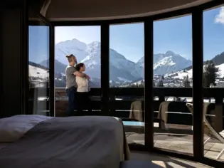 Ein Paar steht vor einem großen Fenster mit Blick auf eine verschneite Berglandschaft.