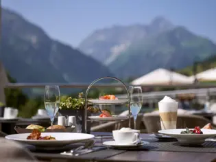 Tisch im Freien mit Geschirr, darunter Teller und Getränke, in einer Berglandschaft.