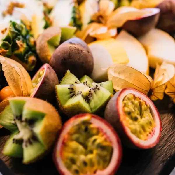 Ein frisches Obstbuffet mit aufgeschnittenen Passionsfrüchten, sternförmig geschnittenen Kiwis, Ananas und Melone im Hintergrund.