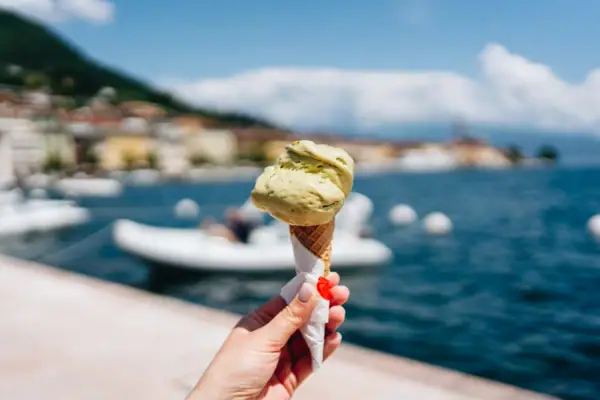 Eine Hand hält ein Eis in einer Waffel mit einem Boot im Hintergrund.