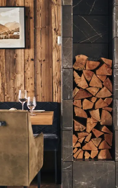 Pile of wood in a niche by the fireplace next to a set table in front of a wood-paneled wall.