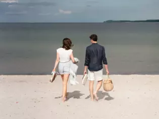 Ein Paar spaziert mit ihren Sachen in der Hand entlang des Strandes. 