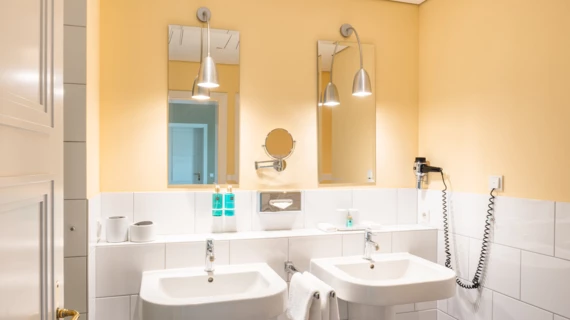 Ein Badezimmer mit zwei Waschbecken und zwei schmalen Spiegeln, die an einer gelben Wand hängen.