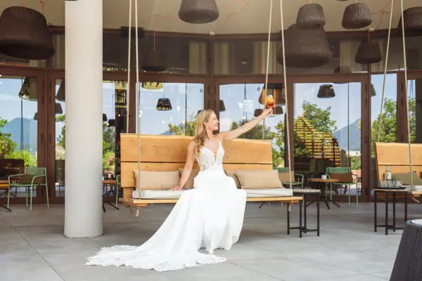 Braut sitzt auf einer Schaukelbank auf der Terrasse mit Blick in den Garten.