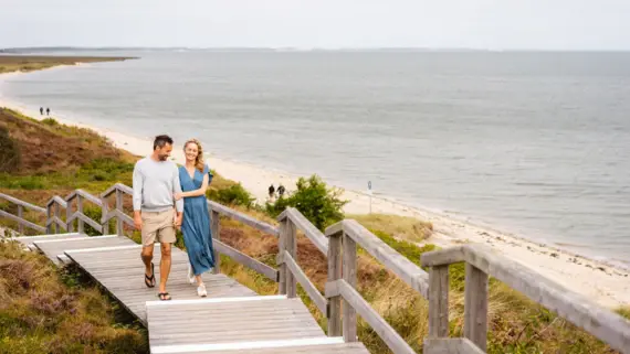 Ein Mann und eine Frau gehen auf einem Holzsteg in der Nähe eines Strandes.