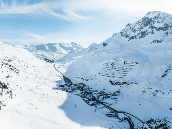 Schneebedeckter Berg mit einer kleinen Dorf im Tal, umgeben von einer winterlichen Landschaft und einem klaren Himmel.