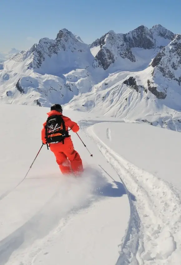 A skier in red clothing with a rucksack on his back is skiing through deep snow.