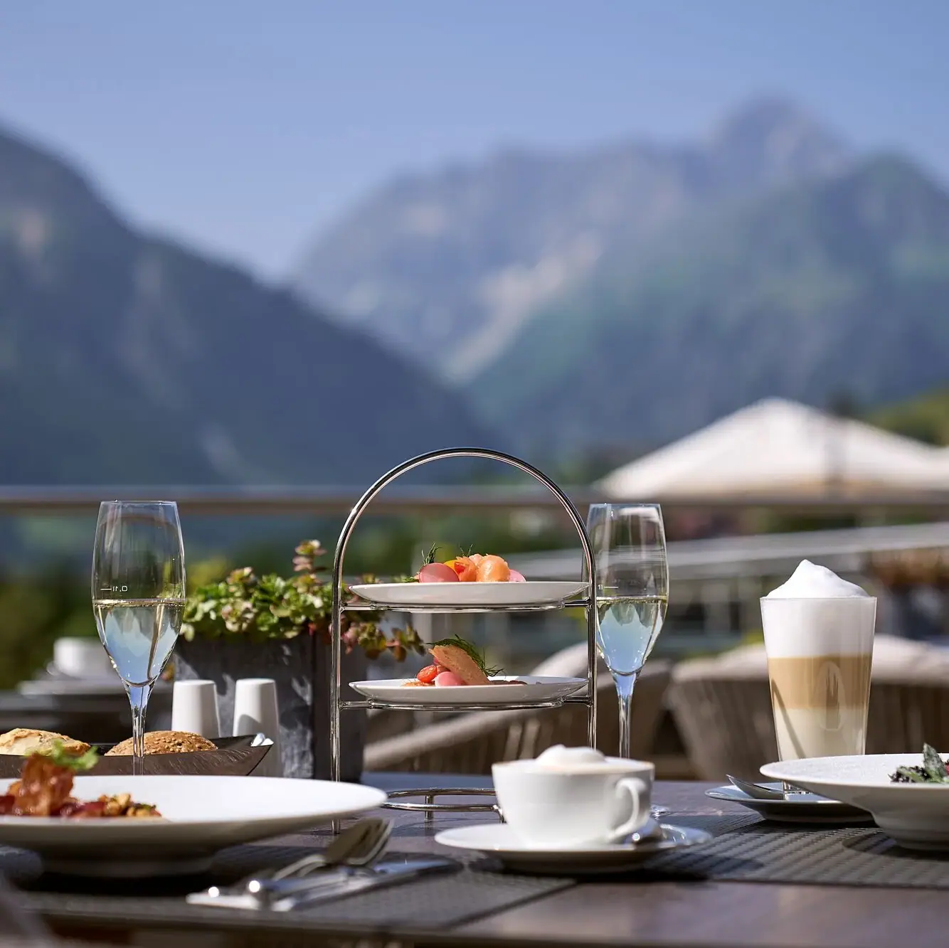 Ein Tisch mit Tellern voller Speisen und Getränken vor einer Bergkulisse mit blauem Himmel..