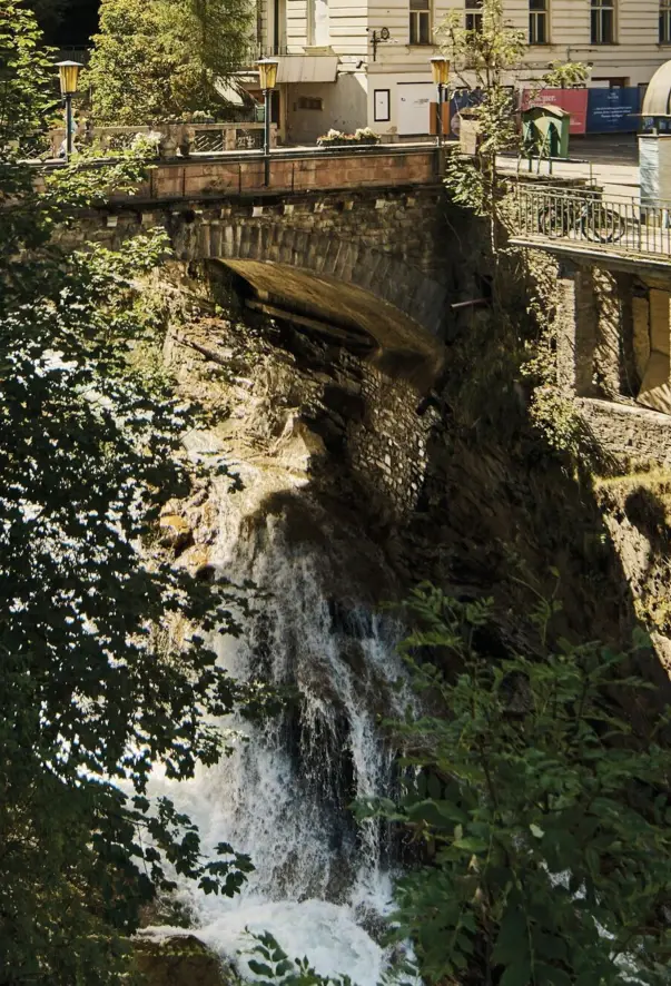 Brücke über einem Abgrund mit einem Wasserfall umgeben von Bäumen.