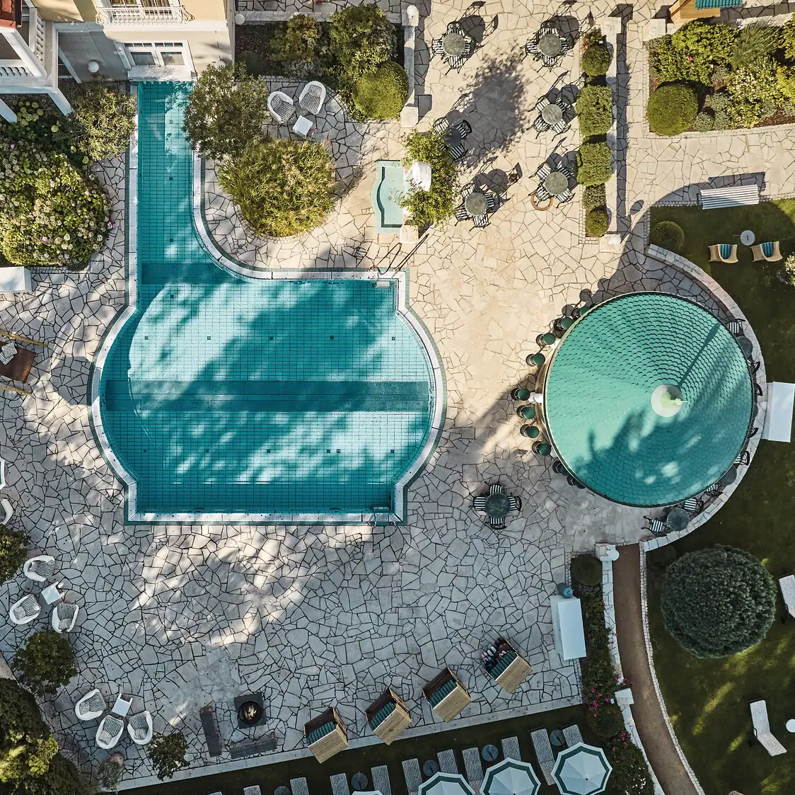 Pool mit Liegestühlen und Bäumen im Hintergrund aus der Vogelperspektive..
