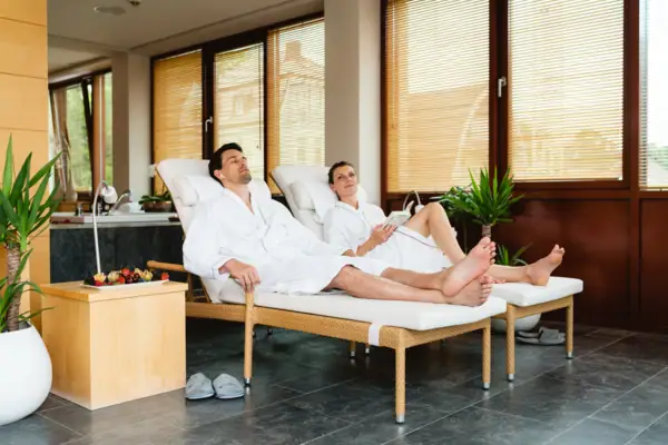 Ein Mann und eine Frau in weißen Bademänteln liegen auf Liegestühlen.