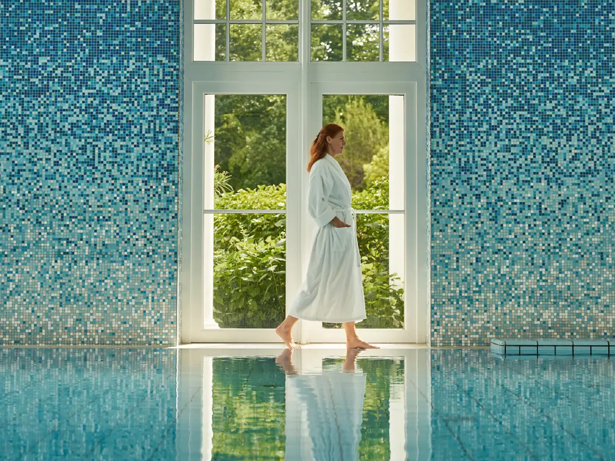 Eine Frau im weißen Bademantel geht in einem Pool.