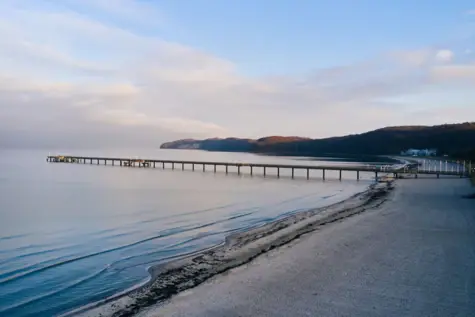 Ein langer Steg reicht in das vom Sonnenuntergang in warme Farben getauchte Ostseewasser. 