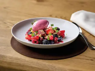 Ein Teller mit fruchtigem Dessert, bestehend aus verschiedenen Beeren und Früchten, serviert mit einem Löffel.