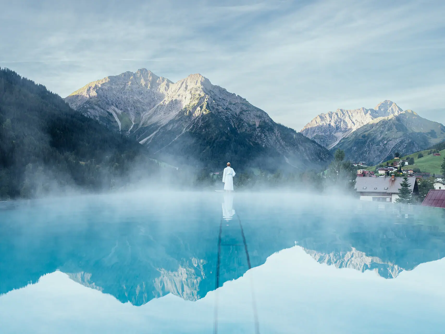 Eine Person steht in einem Pool mit Bergen im Hintergrund.