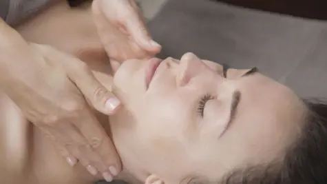 A facial massage during a wellness treatment, with gentle finger movements massaging the forehead of a relaxed woman with her eyes closed. The close-up focuses on the professional strokes of the masseuse, who gently touches the woman's face and creates a calming atmosphere.