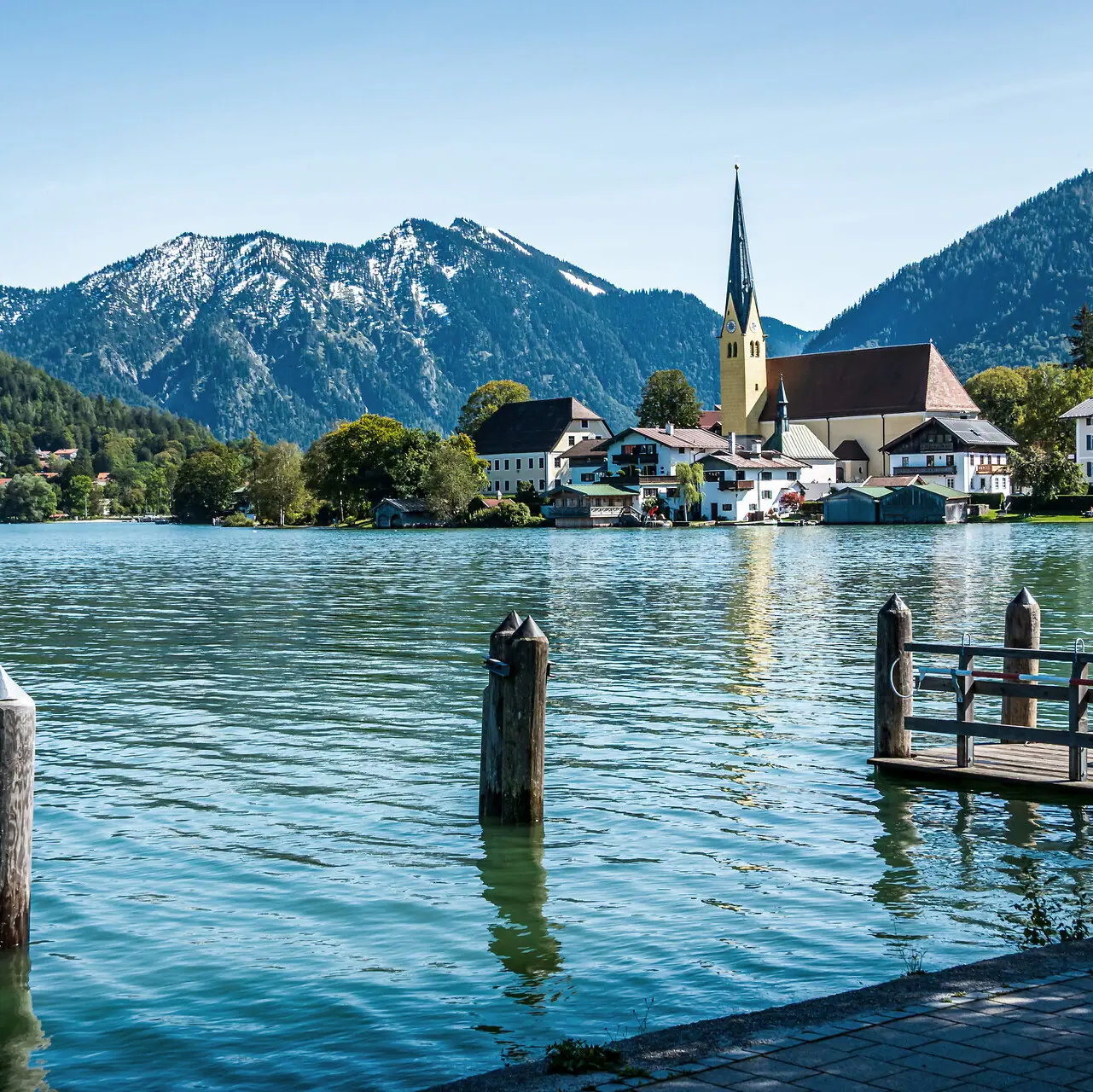 Der Tegernsee mit einer Kirche und Bergen im Hintergrund.