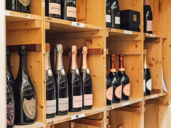A wooden shelf contains many bottles of champagne in different compartments.