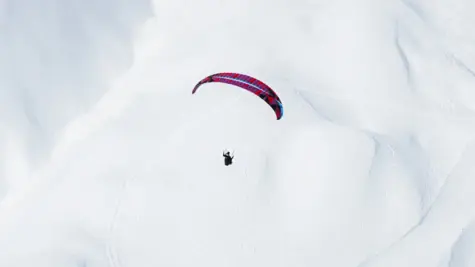 Ein Paraglider schwebt über einer verschneiten Berglandschaft.