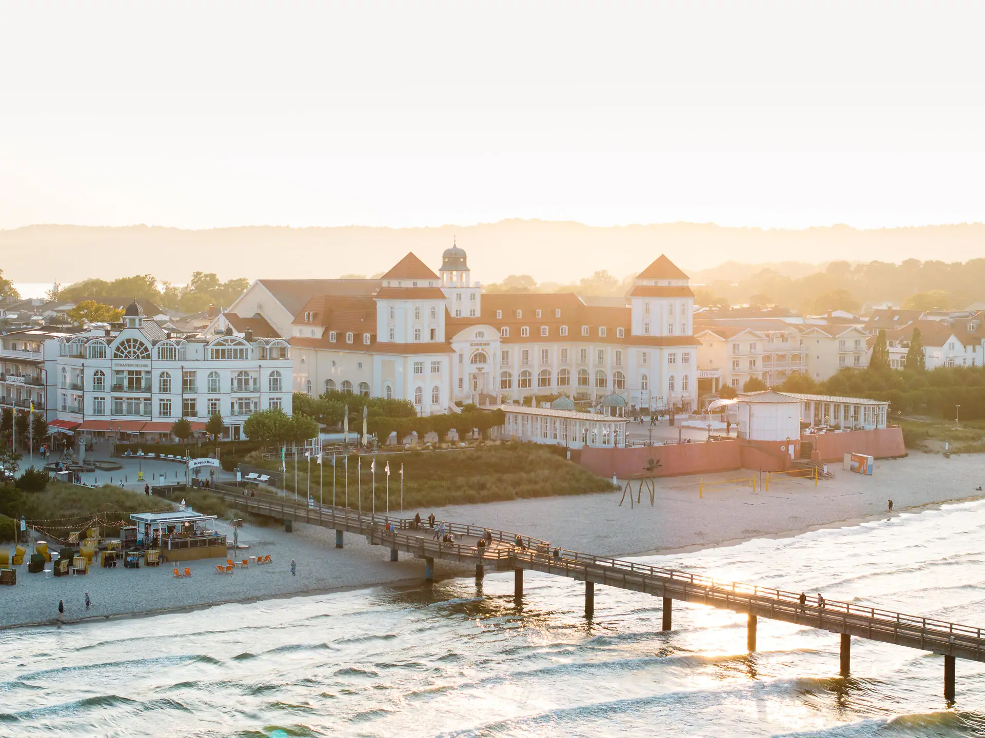 A-ROSA Kurhaus Binz Ein Pier über einem Strand mit Gebäuden und einem Gewässer im Winter.