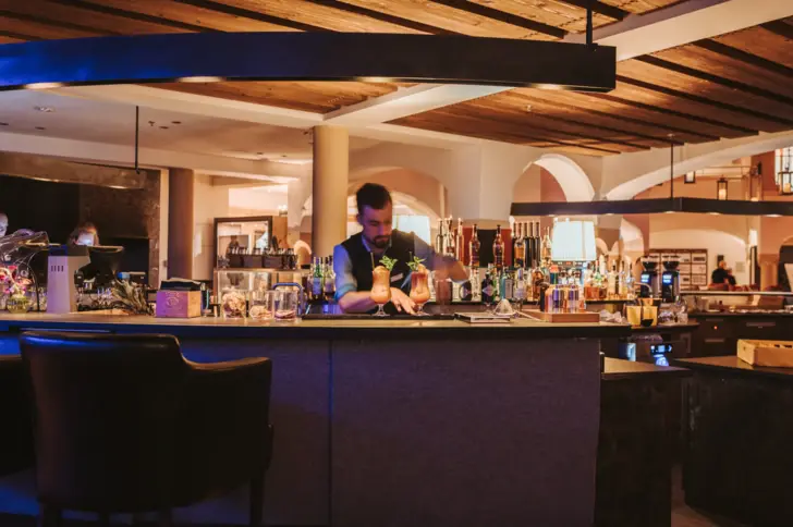 Eine runde, große Bar mit einem Barkeeper in warmem, angenehmen Ambiente. 