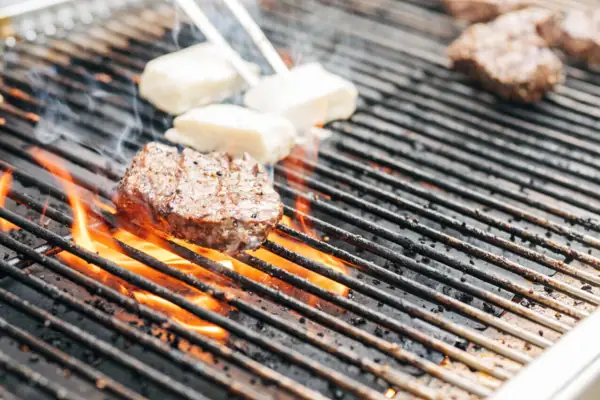 Ein Grill mit Fleisch und Käse darauf während eine Person mit einer Grillzange den Käse wendet.