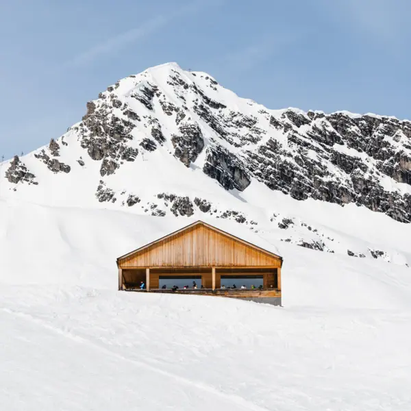 Ein Holzhütte im Schnee, umgeben von einer winterlichen Landschaft mit Bergen.