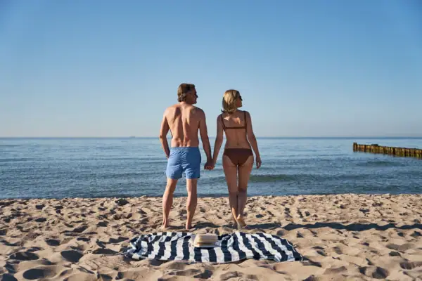 Ein Mann und eine Frau halten sich an einem Strand an den Händen.