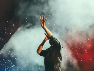 Ein Sänger hebt seine Hand vor einem rauchigen Hintergrund bei einem Konzert.