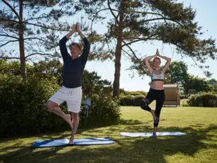 Ein Mann und eine Frau machen Yoga auf Matten in einem Park.