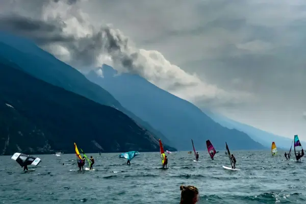 Eine Gruppe von Menschen auf Segelbrettern auf dem Wasser mit Bergen im Hintergrund.