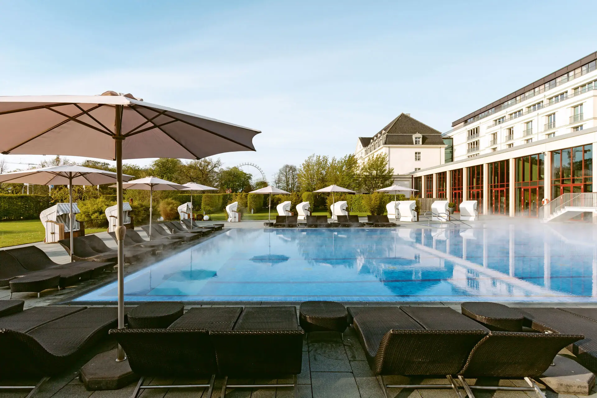 Großes weißes Gebäude mit Pool und Bäumen im Vordergrund.