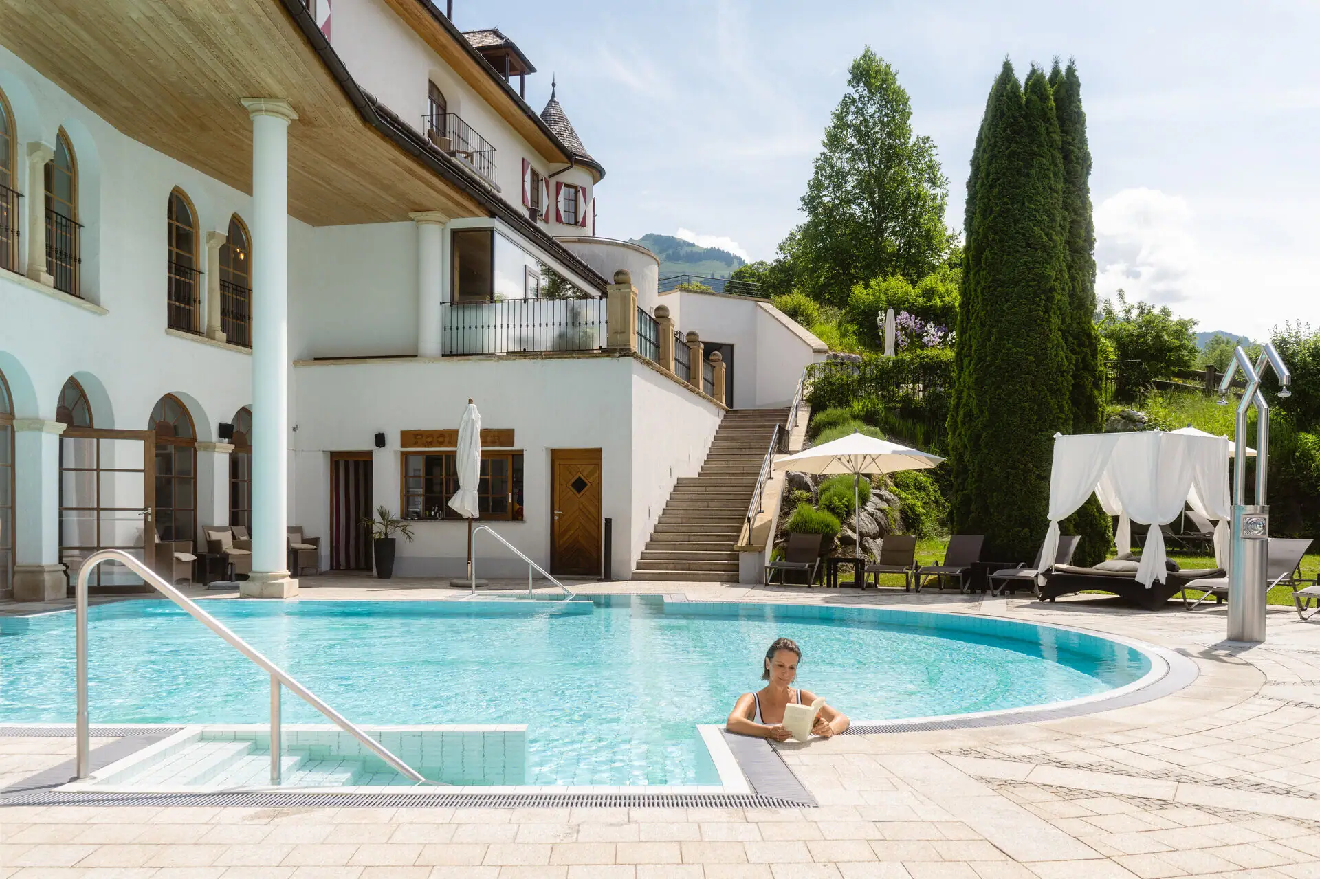 Frau im Pool mit weißem Gebäude und Bäumen im Hintergrund