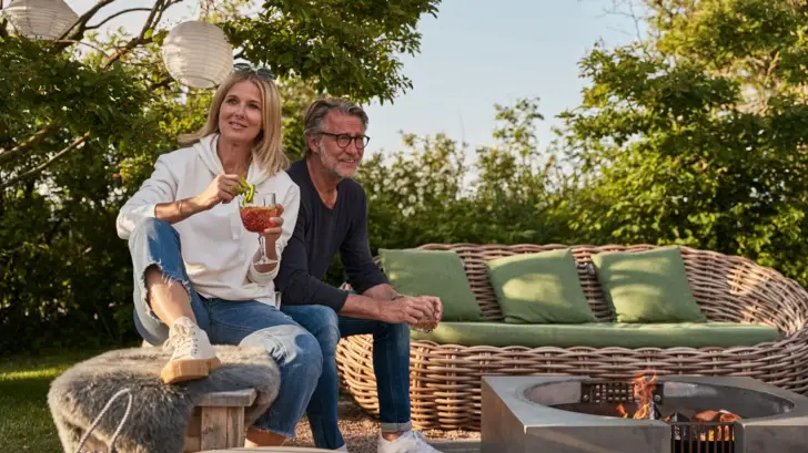 Ein Mann und eine Frau sitzen auf einer Bank im Freien und halten Getränke.