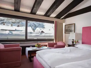Ein Hotelzimmer mit einem roten Bett und zwei roten Sesseln, die vor einem großen Panoramafenster stehen.