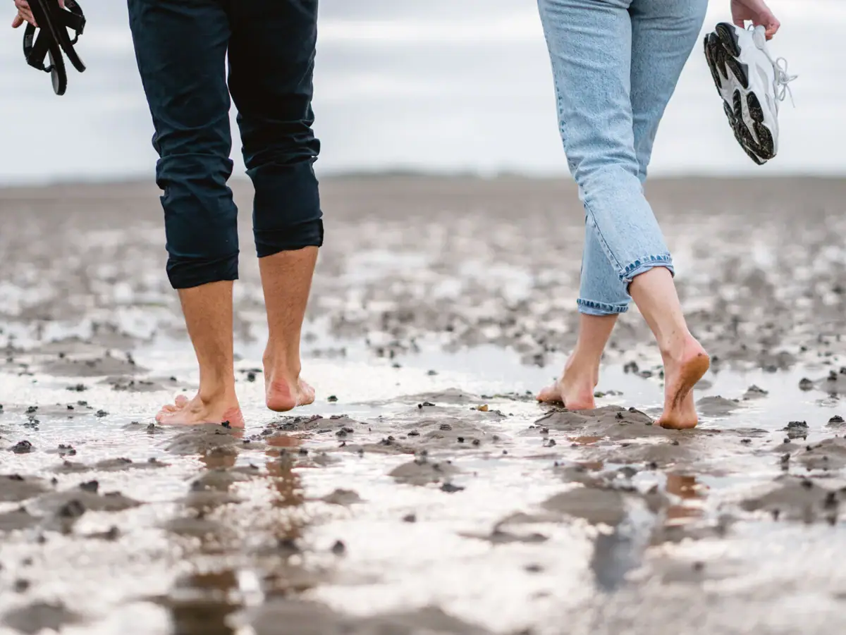 Wattwanderung Sylt Ein Mann und eine Frau machen eine Wattwanderung und gehen barfuß auf nassem Sand.