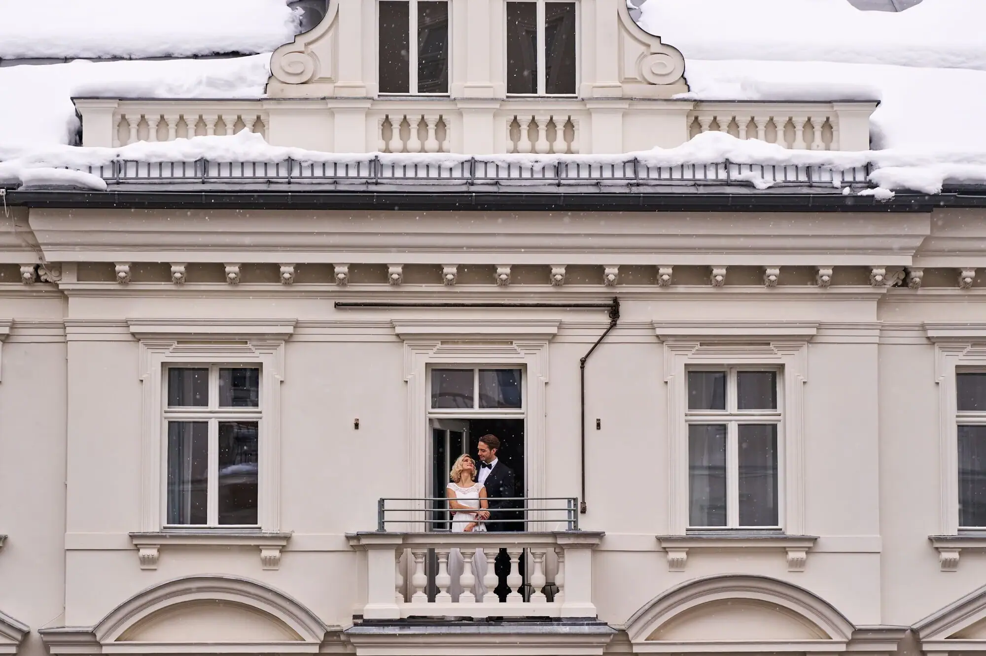 Ein Mann und eine Frau stehen auf einem Balkon vor einem Gebäude.